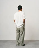 Back view of a model wearing a white Gramicci Ladybug Tee and light green pants on a light-tone background.