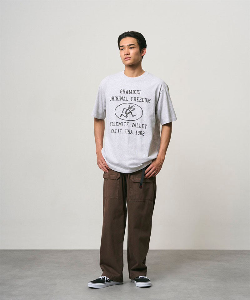 Model wearing a ash heather colored Gramicci Yosemite Valley Tee with a graphic and brown pants on a light-tone background.