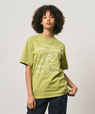 Model wearing a Gramicci sweet pea colored Yosemite Valley Tee with a graphic against a light-tone background.
