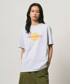 Model wearing a Gramicci ash heather colored Starburst Tee with a graphic against a light-tone background.