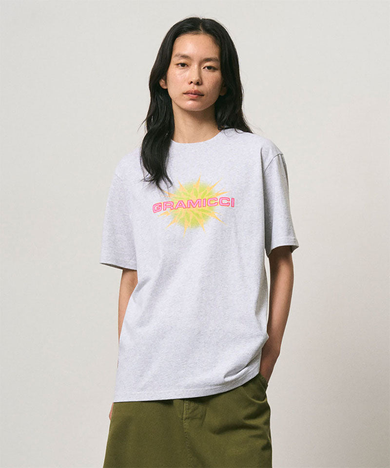 Model wearing a Gramicci ash heather colored Starburst Tee with a graphic against a light-tone background.