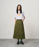 Model wearing a ash heather colored Gramicci Starburst Tee with a graphic and olive skirt on a light-tone background.