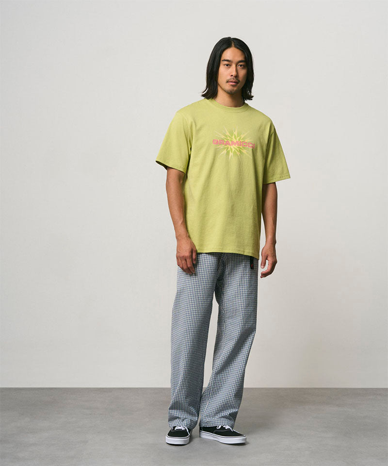 Model wearing a sweet pea colored Gramicci Starburst Tee with a graphic and grey pants on a light-tone background.