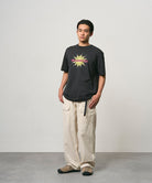Model wearing a vintage black Gramicci Starburst Tee with a graphic and creme colored pants on a light-tone background.