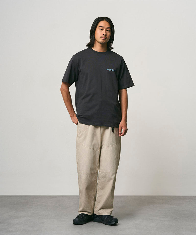 Model wearing a vintage black Gramicci Joker Tee with a teal graphic and beige pants on a light-tone background.