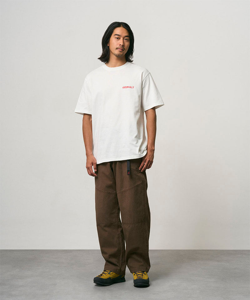 Model wearing a white Gramicci Joker Tee and light green pants on a light-tone background.