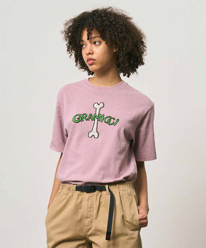 Model wearing a Gramicci lailac pigment colored Bone Tee Pigment Dyed with a graphic against a light-tone background.