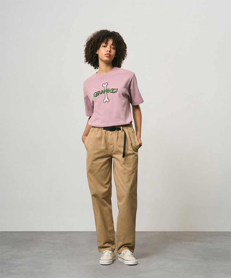 Model wearing a lailac pigment colored Gramicci Bone Tee Pigment Dyed with a graphic and beige pants on a light-tone background.