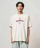 Model wearing a Gramicci natural pigment colored Bone Tee Pigment Dyed with a graphic against a light-tone background.