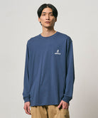 Model wearing a Gramicci dusky blue One Point Logo Long Sleeve Tee with a graphic against a light-tone background.