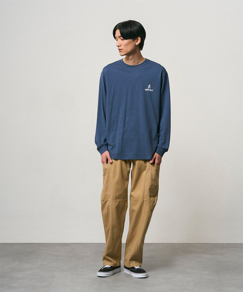 Model wearing a dusky blue Gramicci One Point Logo Long Sleeve Tee with a graphic and beige pants on a light-tone background.