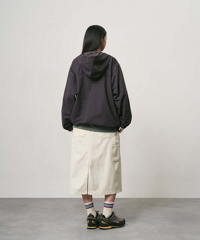 Back view of a model wearing a bone colored Gramicci Denim Carpenter Skirt and a dark brown jacket on a light-tone background.