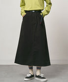 Model wearing a black Gramicci 5-Pocket Skirt and a brown vest on a light-tone background.