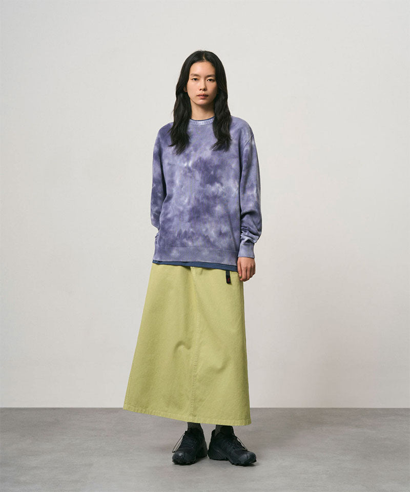 Model wearing a elm pigment colored Gramicci 5-Pocket Skirt and a purple tie-dye sweatshirt on a light-tone background.