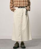 Model wearing a greige colored Gramicci 5-Pocket Skirt and a brown plaid shirt on a light-tone background.