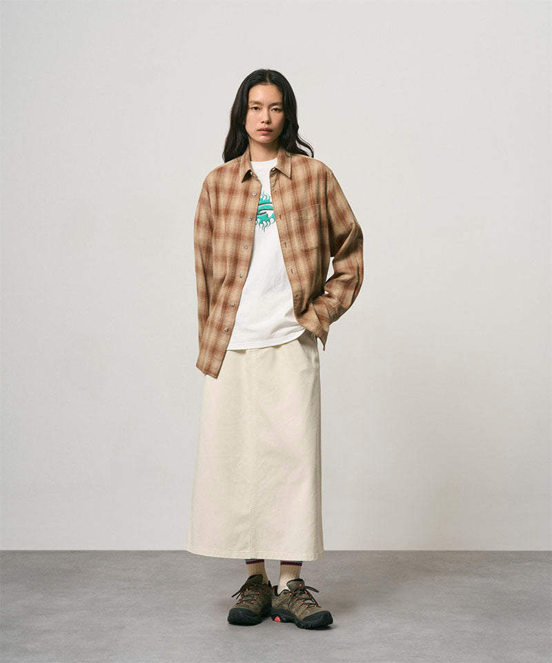 Model wearing a greige colored Gramicci 5-Pocket Skirt and a brown plaid shirt on a light-tone background.