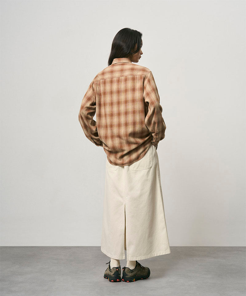 Back view of a model wearing a greige colored Gramicci 5-Pocket Skirt and a brown plaid shirt on a light-tone background.