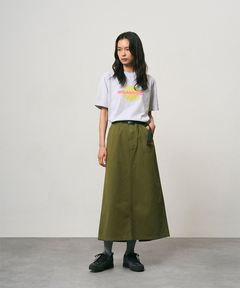 Model wearing a olive colored Gramicci 5-Pocket Skirt and a white shirt on a light-tone background.