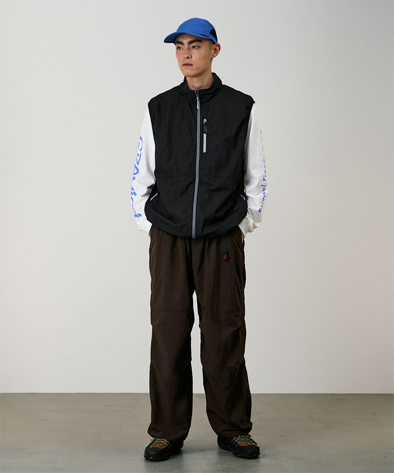 Model wearing a black Gramicci Flyweight Vest and brown pants on a light-tone background.