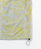 Gramicci yellow and grey grid camo Flyweight Vest hem detail with drawstring against a light-tone background.