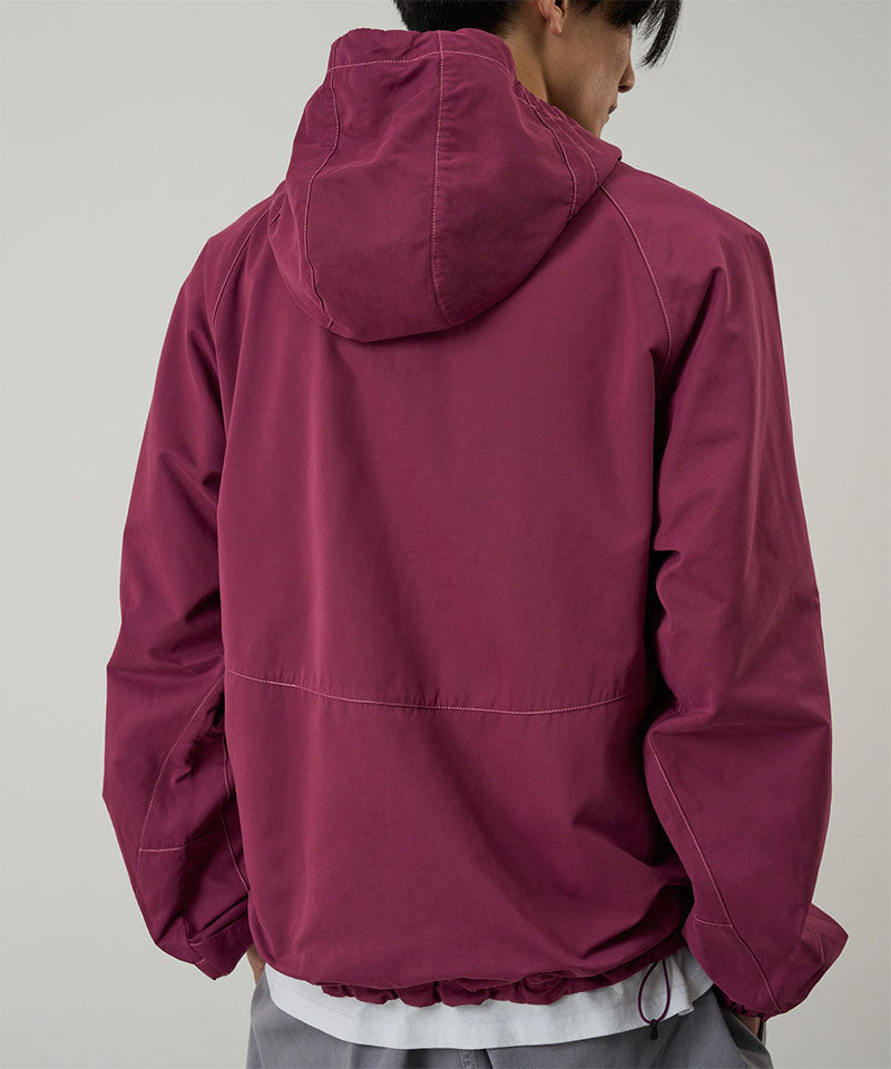Back view of a model wearing a Gramicci burgundy Milton Hooded Jacket against a light-tone background.