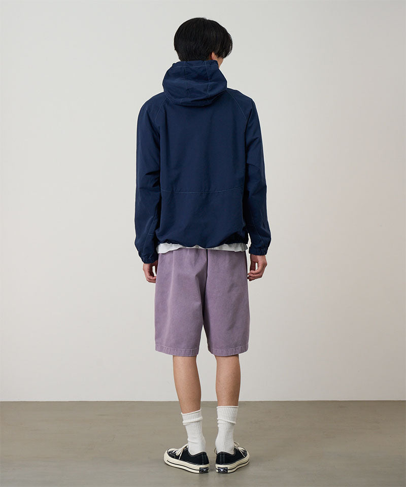 Back view of a model wearing a dark navy Gramicci Milton Hooded Jacket and purple shorts on a light-tone background.