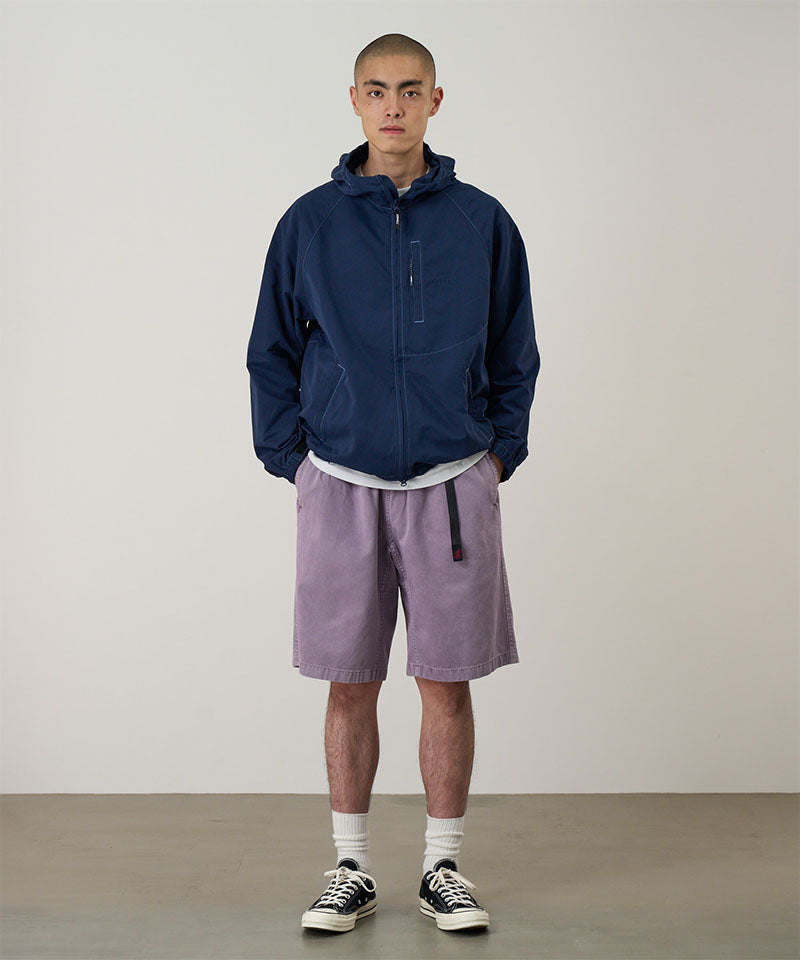Model wearing a Gramicci Natural Dyed Jam Short in the color purple and a blue hoodie on a light-tone background.
