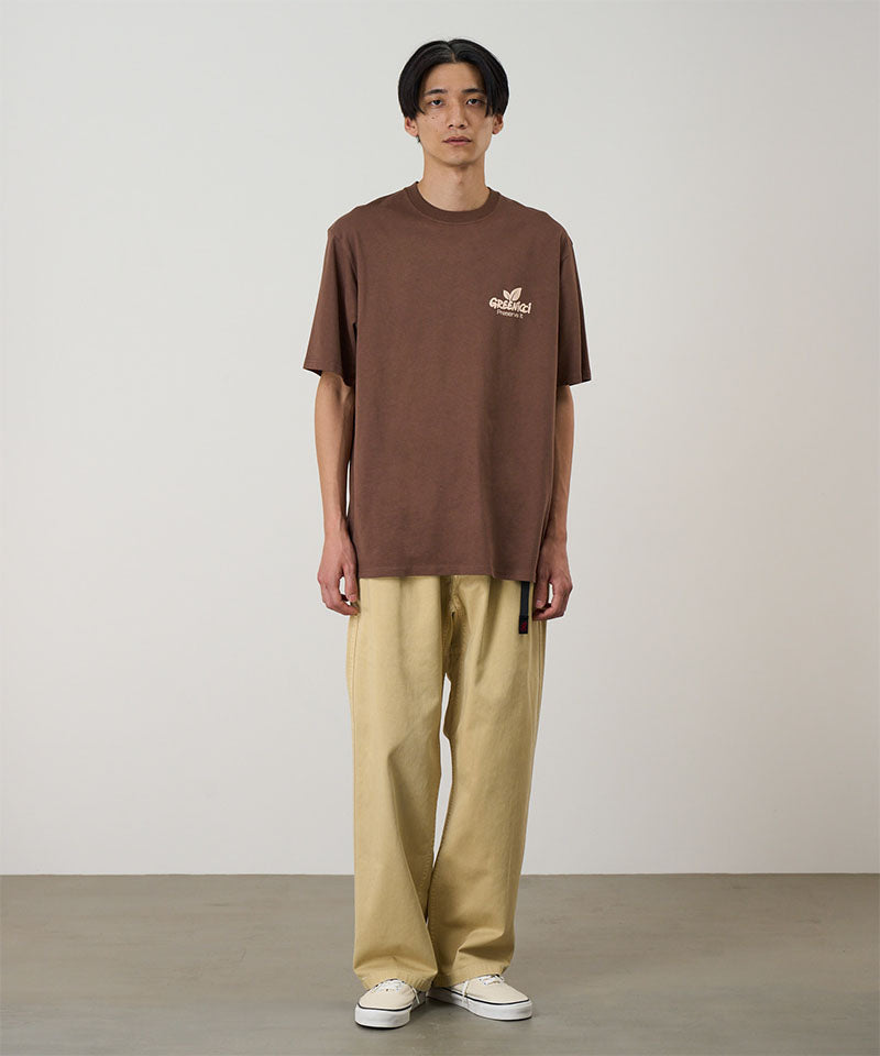 Model wearing a Natural Dyed Gramicci Pant Straight Fit in chino and brown shirt on a light-tone background.

