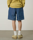 Back view of a model wearing blue Gramicci Japanese Chambray Shorts and a yellow shirt on a light-tone background.