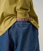 Back view of a model wearing blue Gramicci Japanese Chambray Shorts and a yellow shirt on a light-tone background.