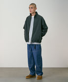 Model wearing the Gramicci Japanese Chambray Double Knee pant in blue and a dark green jacket on a light tone background.
