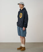 Model wearing a blue multistripe Gramicci Gramicci O.G. G-Short Seersucker Plaid with grey and green graphic and navy hoodie on a light-tone background.