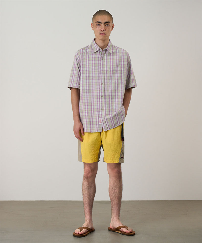 Model wearing banana colored Gramicci Nylon Block Shorts and a purple plaid shirt on a light-tone background.