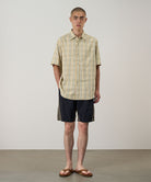 Model wearing black Gramicci Nylon Block Shorts and a yellow plaid shirt on a light-tone background.