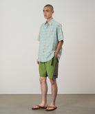 Model wearing jade green Gramicci Nylon Block Shorts and a green plaid shirt on a light-tone background.