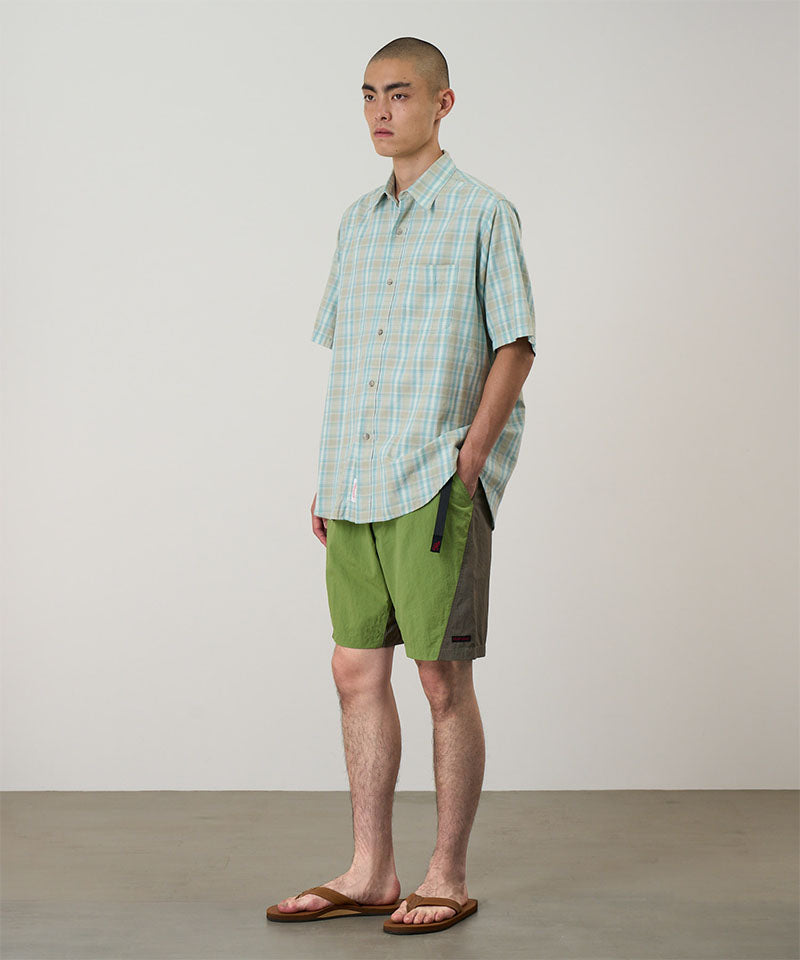 Model wearing jade green Gramicci Nylon Block Shorts and a green plaid shirt on a light-tone background.