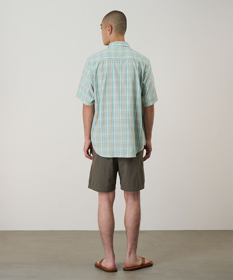 Back view of a model wearing jade green Gramicci Nylon Block Shorts and a green plaid shirt on a light-tone background.