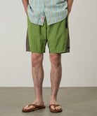 Model wearing jade green Gramicci Nylon Block Shorts and a green plaid shirt on a light-tone background.
