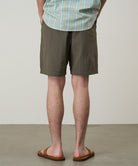 Back view of a model wearing jade green Gramicci Nylon Block Shorts and a green plaid shirt on a light-tone background.