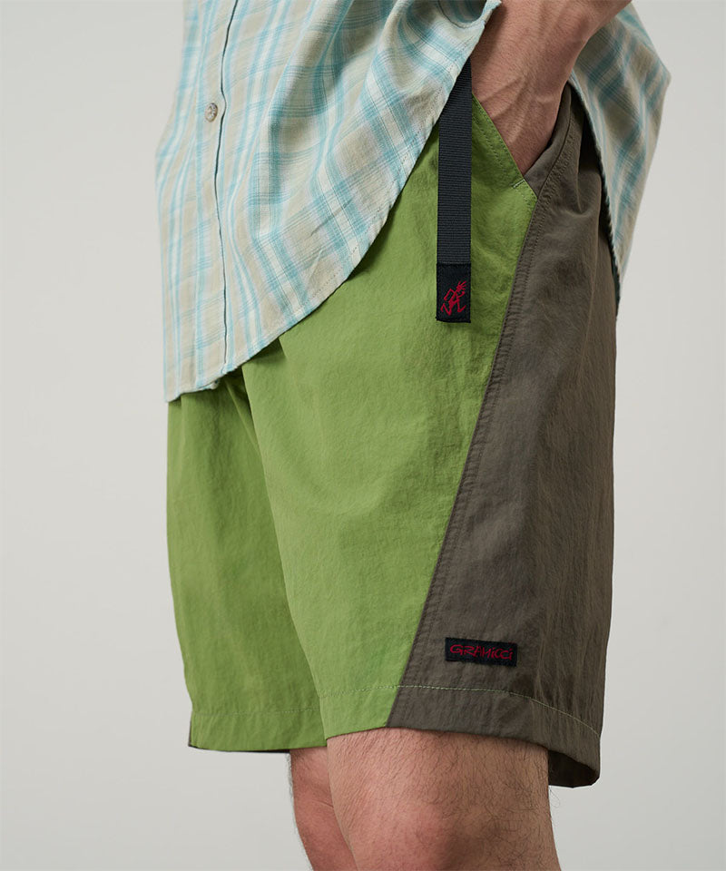 Back view of a model wearing jade green Gramicci Nylon Block Shorts and a green plaid shirt on a light-tone background.