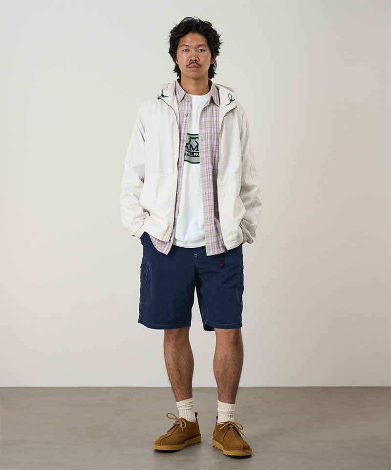 Model wearing british navy Gramicci Nylon Cliff Short and a white jacket on a light-tone background.