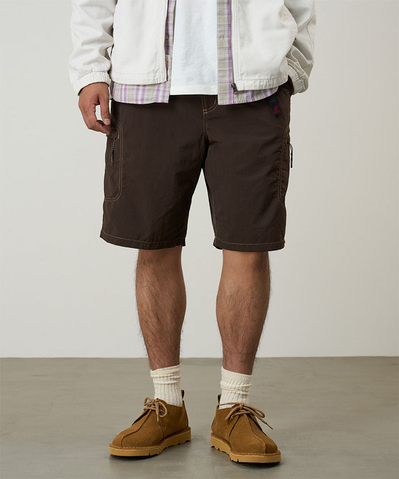 Model wearing chocolate colored Gramicci Nylon Cliff Short and a white jacket on a light-tone background.