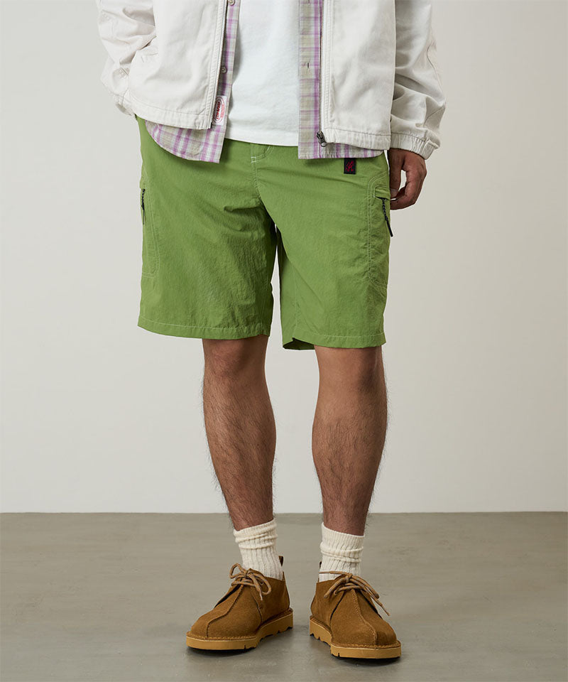 Model wearing jade green Gramicci Nylon Cliff Short and a white jacket on a light-tone background.