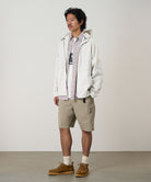 Model wearing milk tea colored Gramicci Nylon Cliff Short and a white jacket on a light-tone background.
