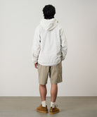 Back view of a model wearing milk tea colored Gramicci Nylon Cliff Short and a white jacket on a light-tone background.