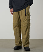 Model wearing khaki Gramicci Convertible Cargo Pants and a black shirt on a light-tone background.