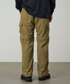 Back view of a model wearing khaki Gramicci Convertible Cargo Pants and a black shirt on a light-tone background.