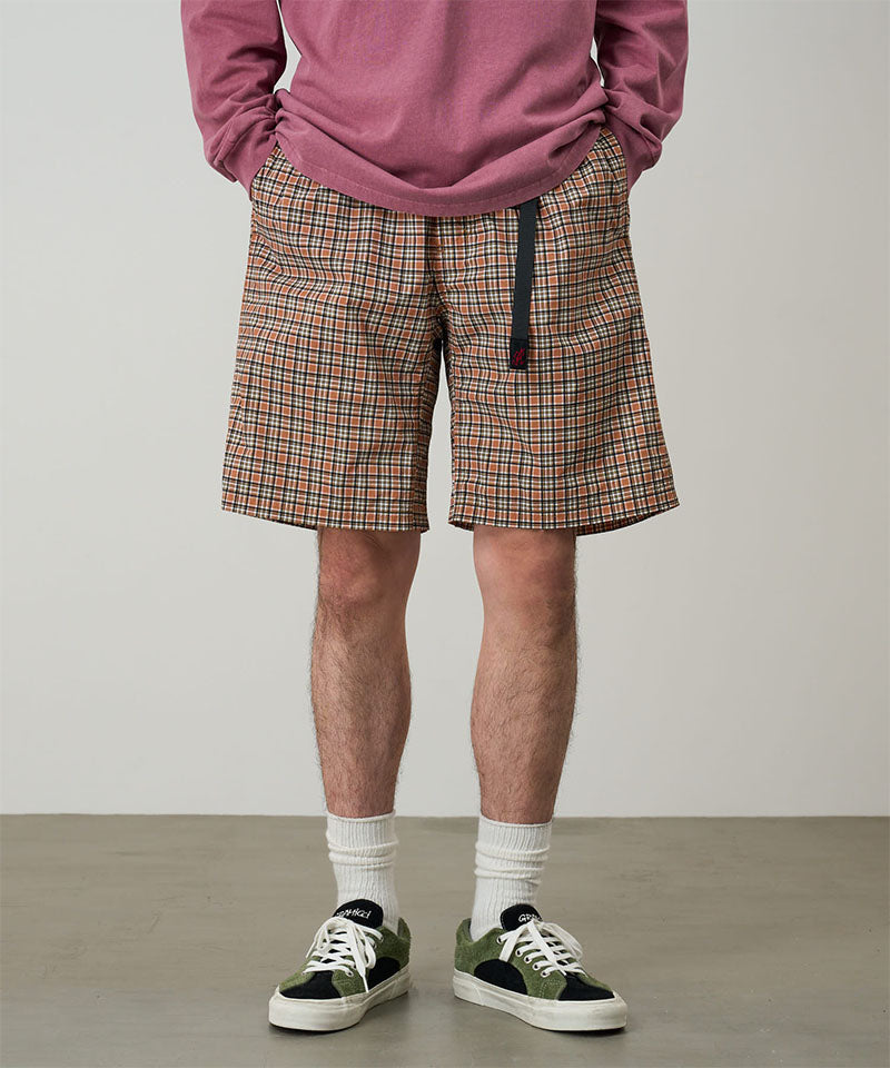 Model wearing brick check colored Gramicci Checkered Shell Shorts and a red shirt on a light-tone background.