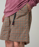 Model wearing brick check colored Gramicci Checkered Shell Shorts and a red shirt on a light-tone background.