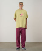 Model wearing burgundy Gramicci Milton Pants and a lime green shirt on a light-tone background.